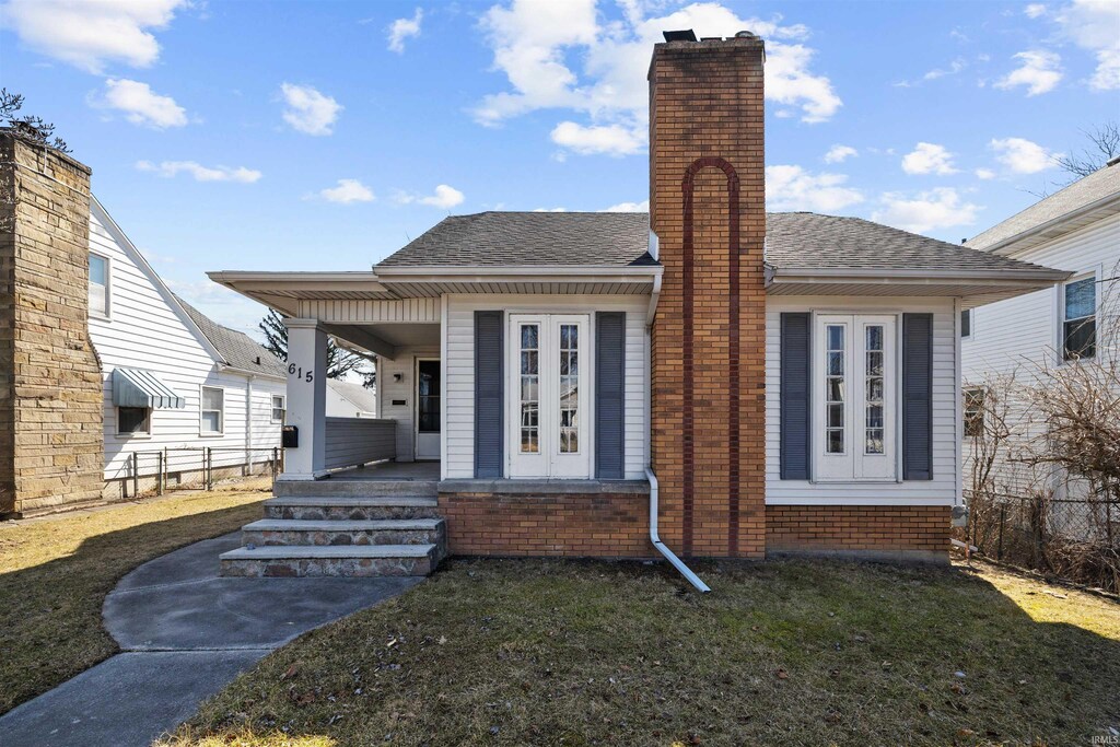 back of property featuring covered porch, a chimney, a lawn, and roof with shingles