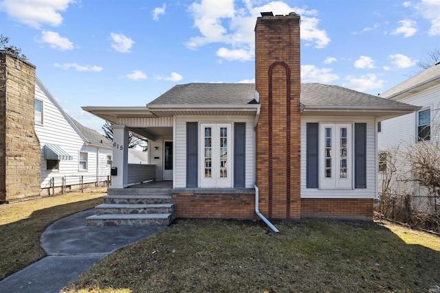 back of property featuring covered porch, a chimney, a lawn, and roof with shingles