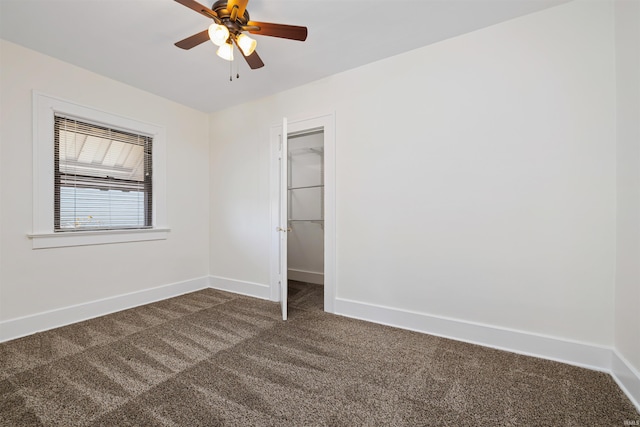 unfurnished bedroom featuring a ceiling fan, baseboards, a closet, a walk in closet, and dark carpet