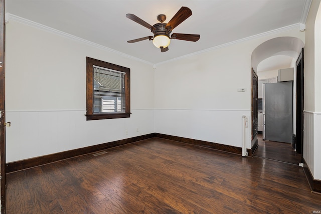 unfurnished room featuring dark wood-type flooring, arched walkways, wainscoting, crown molding, and ceiling fan