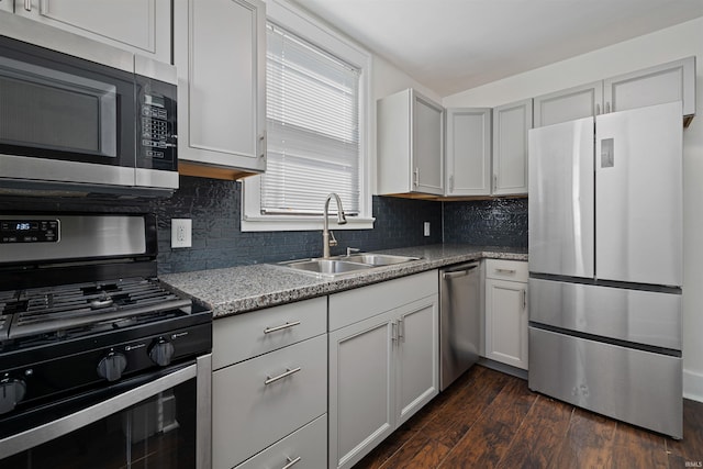 kitchen with a sink, dark wood-style floors, stainless steel appliances, decorative backsplash, and light stone countertops