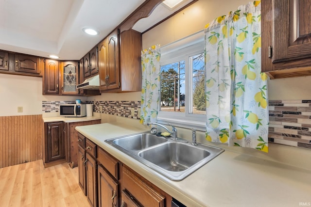 kitchen with a sink, light countertops, light wood-style floors, under cabinet range hood, and backsplash