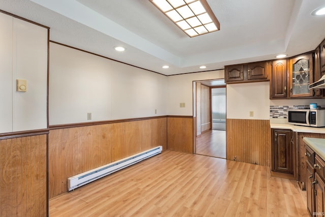 kitchen featuring a wainscoted wall, a baseboard radiator, light countertops, light wood-style floors, and stainless steel microwave