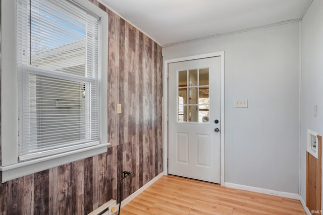 doorway with baseboards, a healthy amount of sunlight, wood walls, and light wood finished floors