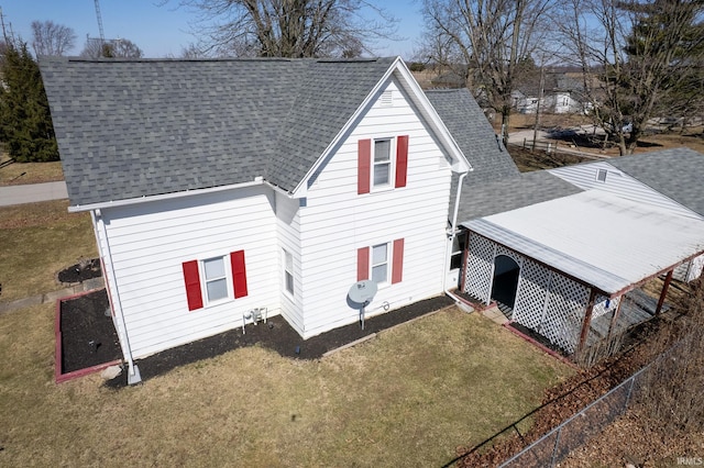 back of property with a shingled roof, a yard, and fence