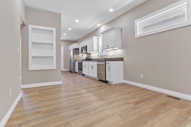 kitchen with baseboards, visible vents, light wood-style flooring, stainless steel appliances, and dark countertops