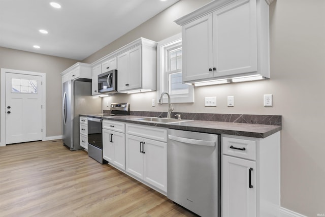 kitchen with a sink, dark countertops, light wood-style floors, appliances with stainless steel finishes, and white cabinets