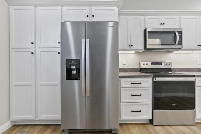 kitchen featuring white cabinetry, dark countertops, light wood-style floors, and stainless steel appliances