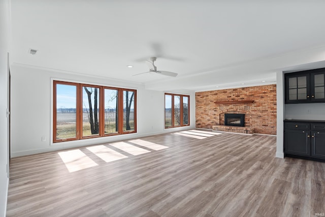 unfurnished living room with a brick fireplace, light wood-style flooring, baseboards, and ceiling fan