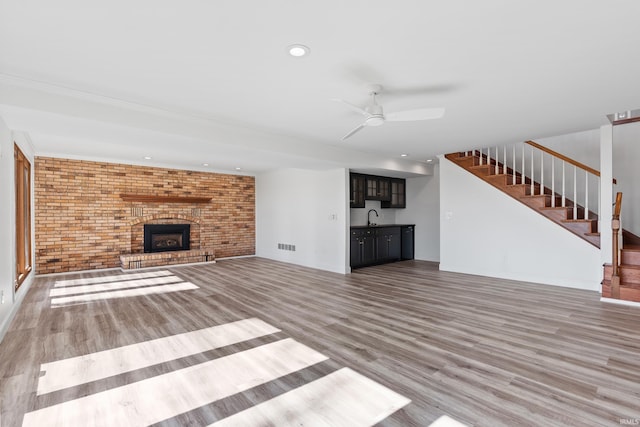 unfurnished living room with a sink, wood finished floors, brick wall, ceiling fan, and stairs