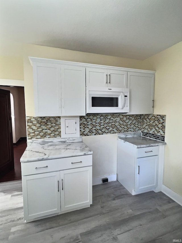 kitchen with white microwave, light wood finished floors, decorative backsplash, light countertops, and white cabinets