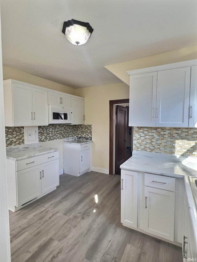 kitchen with white microwave, decorative backsplash, white cabinets, and light wood-type flooring