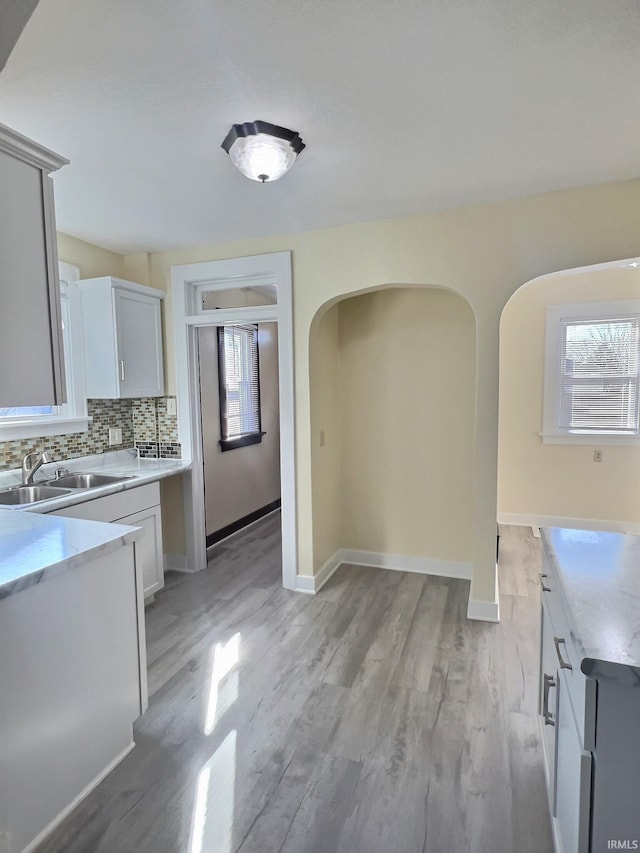 kitchen featuring baseboards, light wood finished floors, arched walkways, a sink, and decorative backsplash