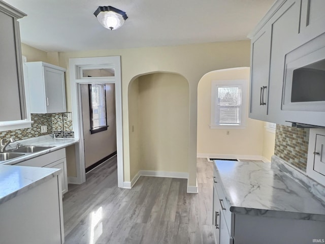 kitchen with light stone counters, white microwave, a sink, light wood-style floors, and tasteful backsplash