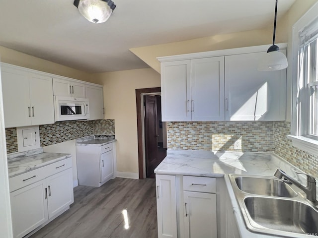 kitchen featuring white microwave, hanging light fixtures, white cabinetry, and a sink