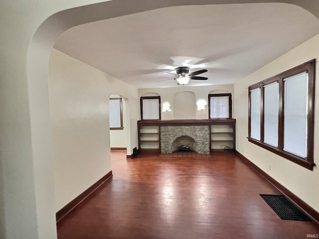 unfurnished living room with visible vents, a stone fireplace, wood finished floors, arched walkways, and a ceiling fan