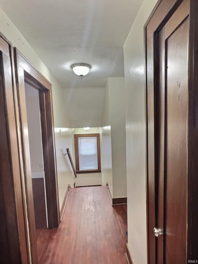 hallway featuring an upstairs landing, a textured ceiling, baseboards, and wood finished floors