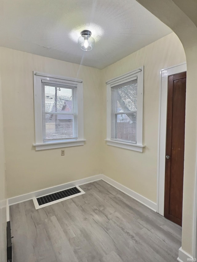 unfurnished room with arched walkways, visible vents, baseboards, and wood finished floors