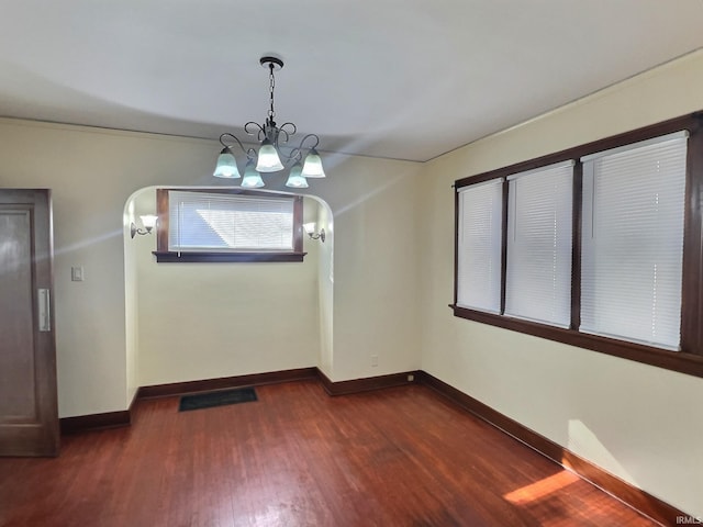 unfurnished dining area with visible vents, dark wood-style floors, arched walkways, baseboards, and a chandelier