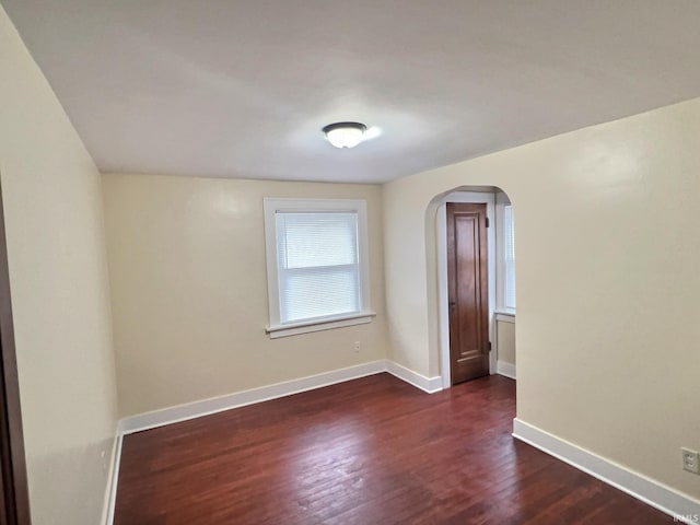 spare room with arched walkways, dark wood-style floors, and baseboards