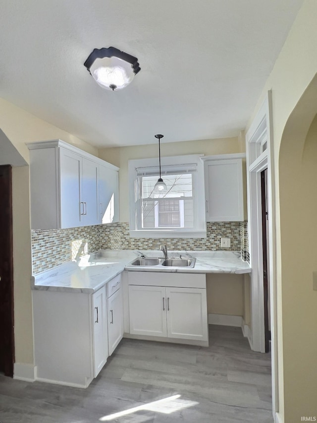 kitchen with a sink, hanging light fixtures, light countertops, white cabinetry, and tasteful backsplash