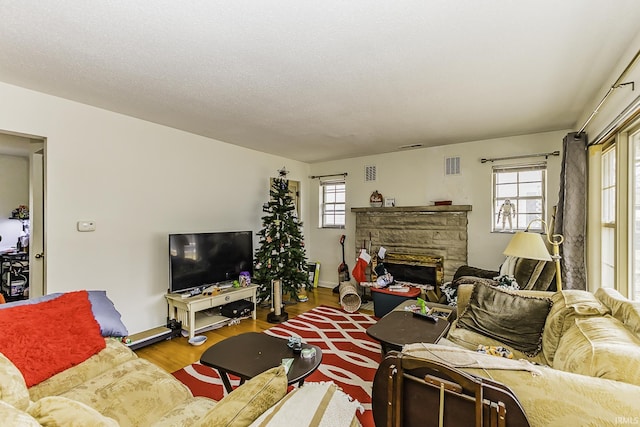 living room with a stone fireplace, wood finished floors, visible vents, and a healthy amount of sunlight