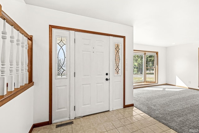 foyer entrance with light tile patterned floors, baseboards, visible vents, and light carpet