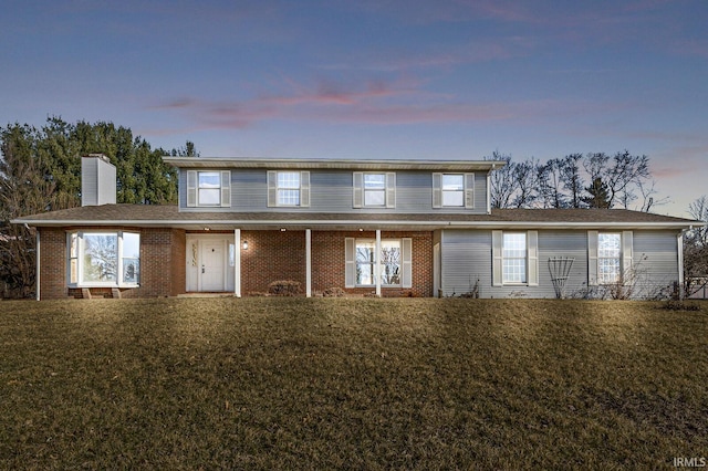 view of front of house featuring brick siding, a chimney, a front yard, and a shingled roof