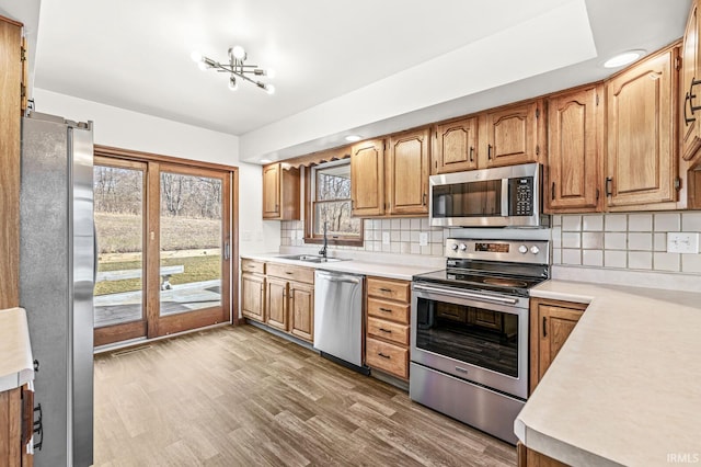 kitchen featuring a sink, tasteful backsplash, wood finished floors, stainless steel appliances, and light countertops