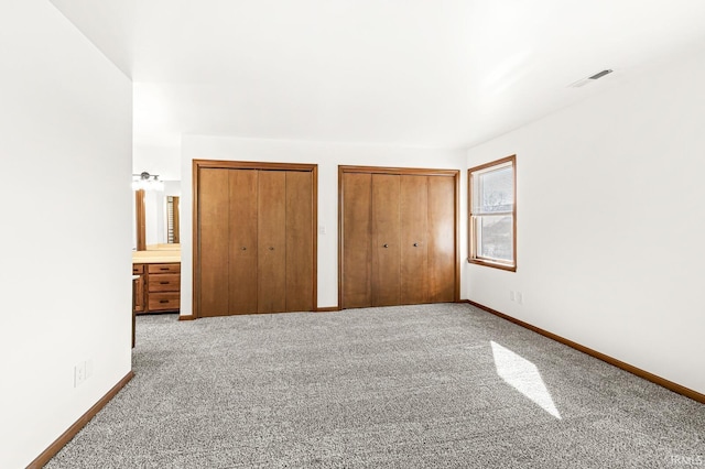 unfurnished bedroom with visible vents, carpet, multiple closets, and baseboards