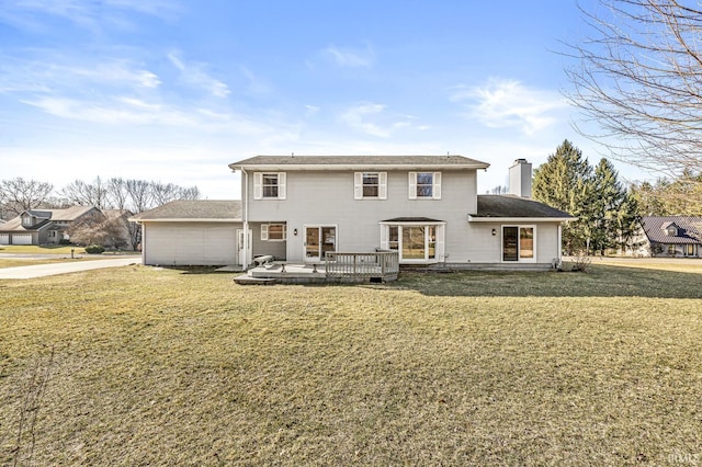 back of property with a deck, a lawn, and a chimney