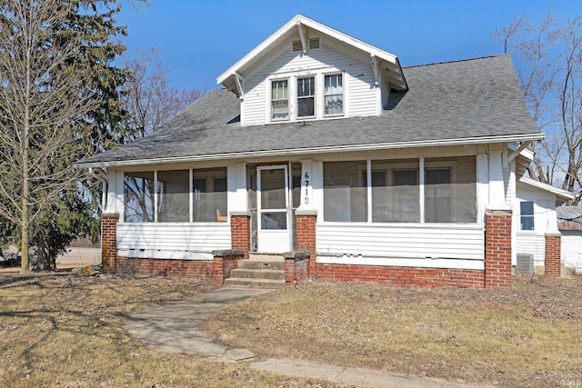 bungalow featuring cooling unit, roof with shingles, a front lawn, and a sunroom