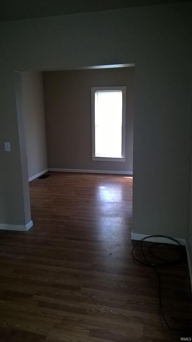 spare room featuring baseboards and dark wood-style flooring