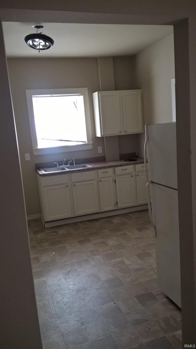 kitchen with white cabinets, freestanding refrigerator, and a sink