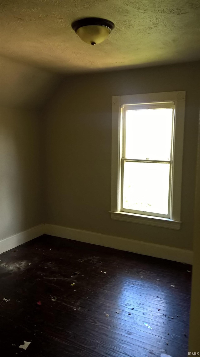 additional living space with baseboards, a textured ceiling, dark wood-style flooring, and vaulted ceiling