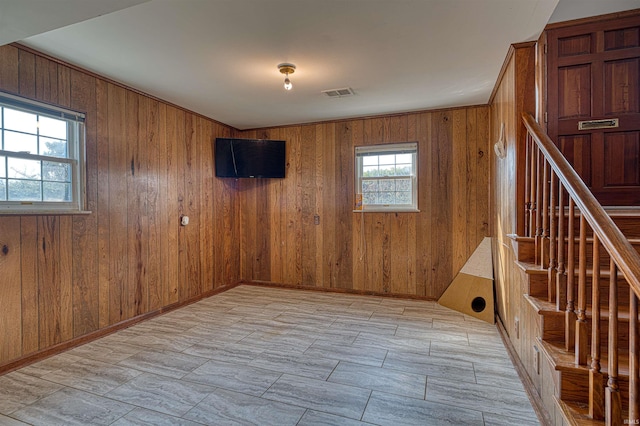 unfurnished room with stairs, wooden walls, baseboards, and visible vents