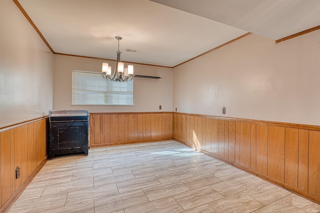 unfurnished dining area with wooden walls, visible vents, ornamental molding, wainscoting, and a notable chandelier