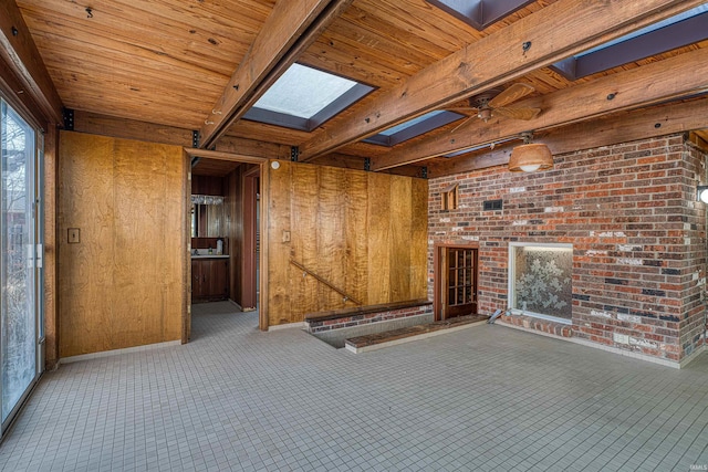 interior space with a ceiling fan, beam ceiling, a skylight, wood ceiling, and wood walls