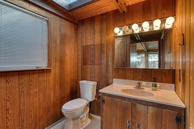 half bath with vanity, tile patterned floors, wooden walls, and toilet