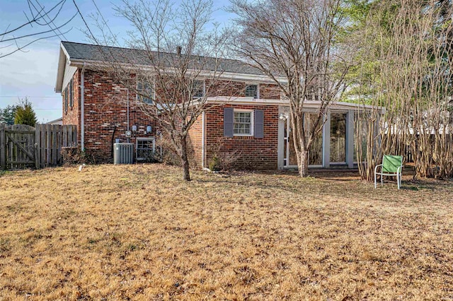 rear view of house with cooling unit, fence, brick siding, and a lawn