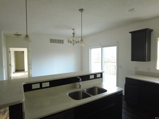 kitchen with visible vents, a chandelier, decorative light fixtures, dark cabinetry, and a sink