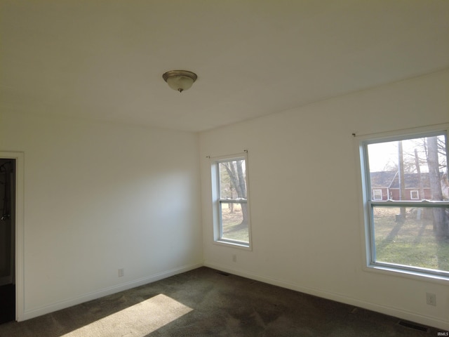 spare room with dark colored carpet, visible vents, and baseboards