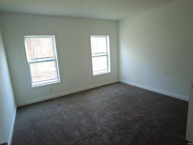 spare room with visible vents, baseboards, and dark colored carpet