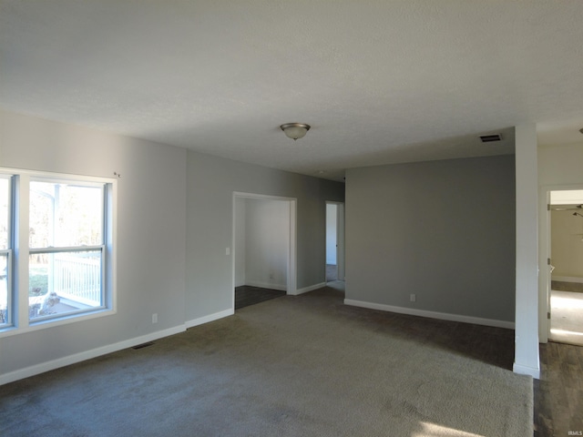 empty room with dark colored carpet, visible vents, and baseboards