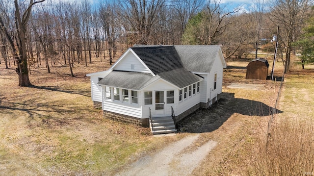 view of front of house featuring dirt driveway, an outdoor structure, and roof with shingles