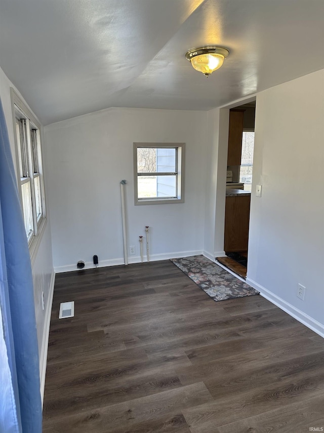 empty room with dark wood finished floors, lofted ceiling, baseboards, and visible vents