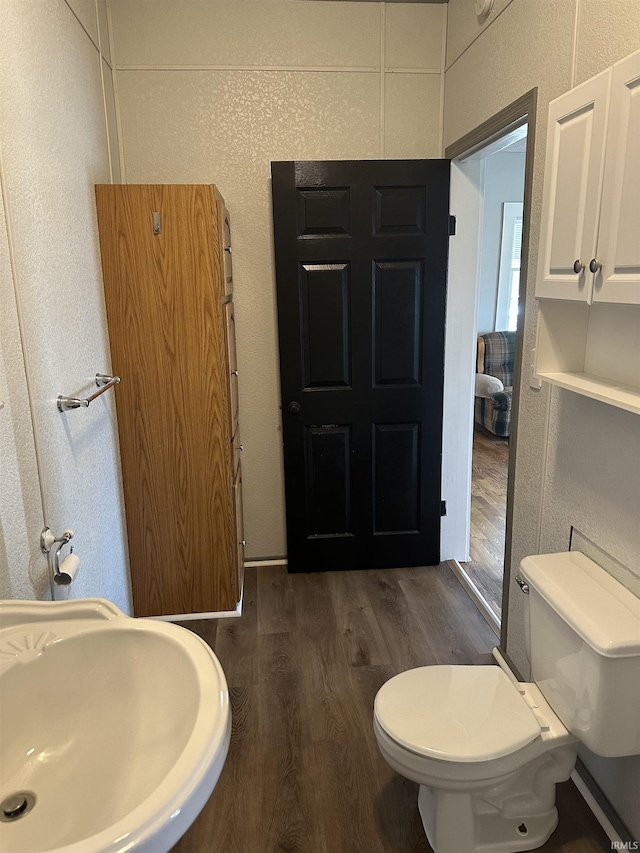 half bath featuring toilet, wood finished floors, a textured wall, and a sink