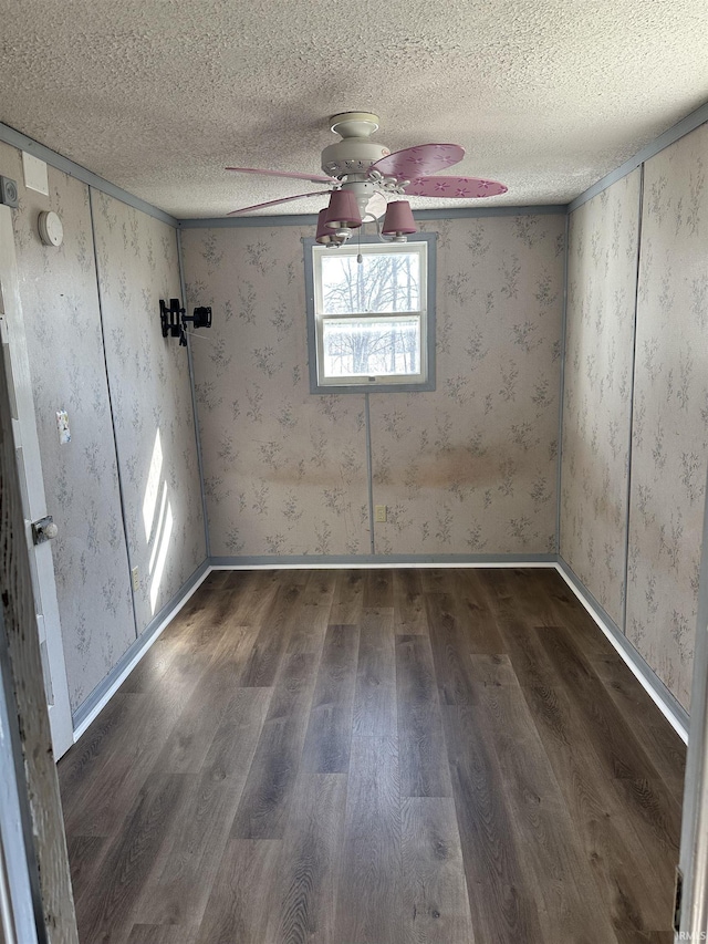 unfurnished room with wood finished floors, a ceiling fan, baseboards, wallpapered walls, and a textured ceiling