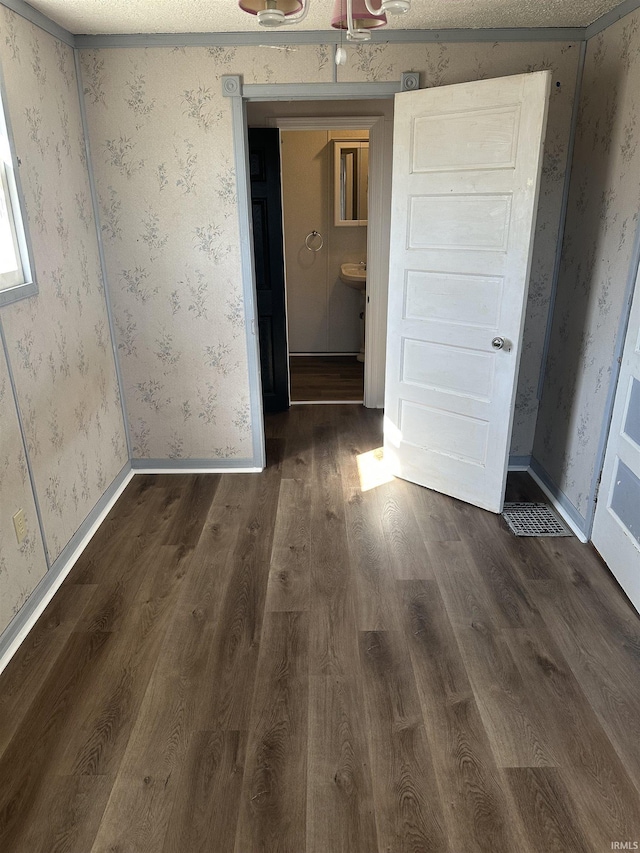 empty room featuring dark wood-style floors, wallpapered walls, and baseboards