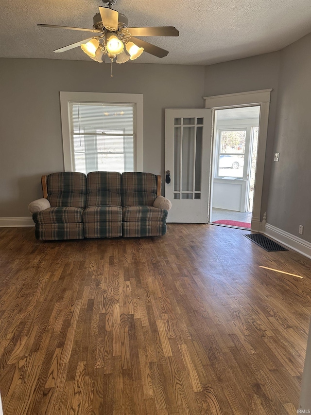 living room featuring a textured ceiling, wood finished floors, baseboards, and ceiling fan